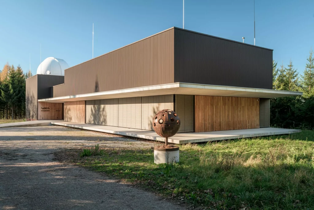 deutinger-projektentwicklung-baumanagement-generalunternehmen-immobilien-salzburg-Sternwarte-Haus-der-Natur-1 Modernes Gebäude der Sternwarte Haus der Natur in Salzburg mit Kugelskulptur im Vordergrund und umgeben von Bäumen
