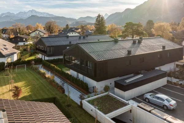 Moderne Wohnanlage mit zwei Gebäuden, Garten, Parkplatz und Bergpanorama im Hintergrund bei Sonnenlicht in Anif bei Salzburg.