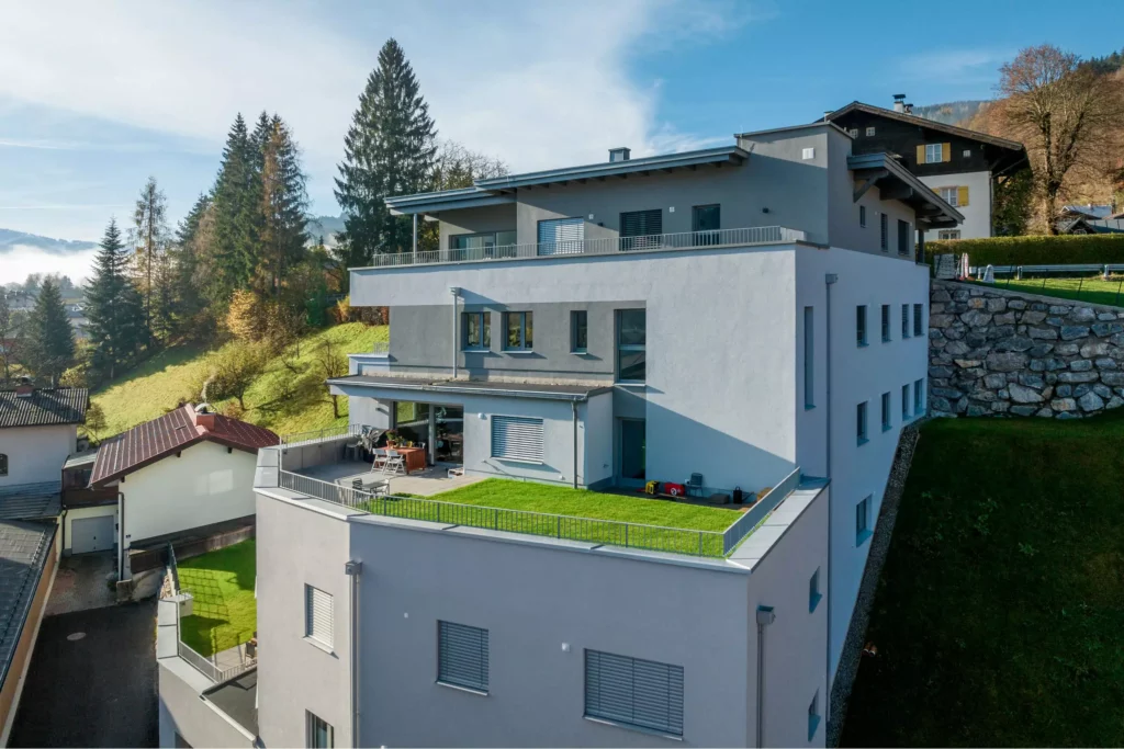 deutinger-projektentwicklung-baumanagement-generalunternehmen-immobilien-salzburg-Wohnpark-Bischofshofen-10 Moderner Wohnpark mit großen Terrassen und Grünflächen in Bischofshofen vor bewaldeten Hügeln und blauem Himmel