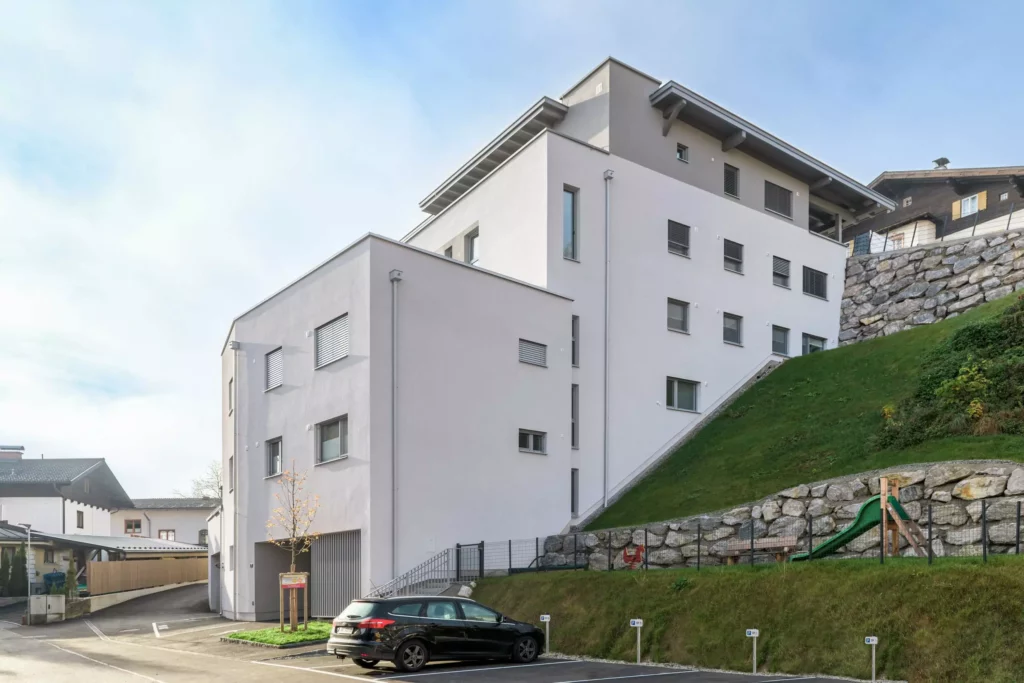 deutinger-projektentwicklung-baumanagement-generalunternehmen-immobilien-salzburg-Wohnpark-Bischofshofen-2 Modernes Wohngebäude mit Parkplätzen und Kinderspielplatz am Hang in Bischofshofen bei Salzburg