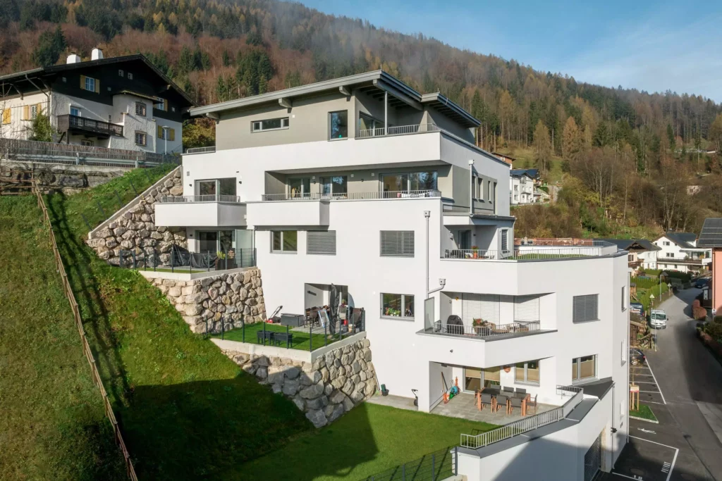 deutinger-projektentwicklung-baumanagement-generalunternehmen-immobilien-salzburg-Wohnpark-Bischofshofen-6 Modernes Wohngebäude mit mehreren Balkonen und Terrassen am Hang vor bewaldetem Berg in Bischofshofen, Salzburg