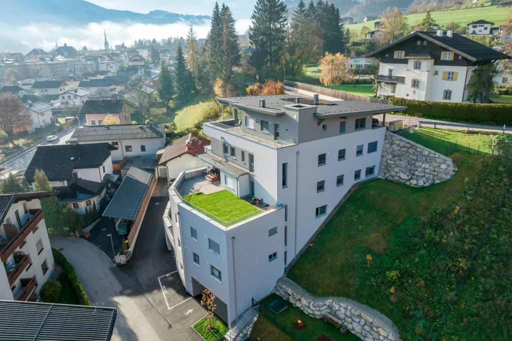 deutinger-projektentwicklung-baumanagement-generalunternehmen-immobilien-salzburg-Wohnpark-Bischofshofen-9 Moderner Wohnpark mit Flachdach und begrüntem Balkon in Bischofshofen, umgeben von Wohnhäusern und grünen Hängen