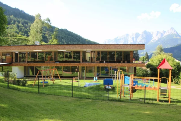 Moderner Kindergarten mit Spielplatz vor Bergkulisse in Salzburg, Beispiel für Bauprojektmanagement und Baumanagement