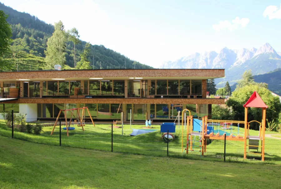 Moderner Kindergarten mit Spielplatz vor Bergkulisse in Salzburg, Beispiel für Bauprojektmanagement und Baumanagement