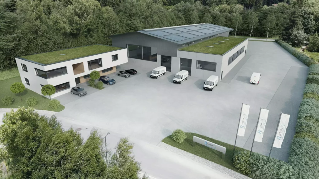 deutinger-projektentwicklung-baumanagement-generalunternehmen-immobilien-salzburg-projekt-betriebshalle-rudek-05 Moderne Betriebshalle mit begrünten Flachdächern, Solarzellen und mehreren Fahrzeugen auf großem Parkplatz in Waldumgebung