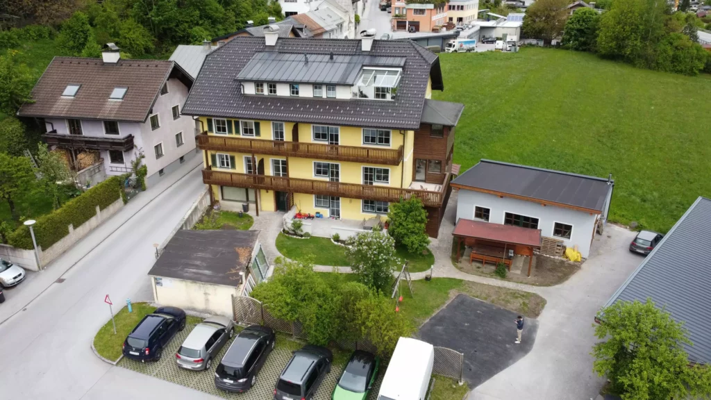 deutinger-projektentwicklung-baumanagement-generalunternehmen-immobilien-salzburg-wohnanlage-werfen64-01 Mehrstöckiges Wohngebäude mit gelber Fassade, Parkplätzen und angrenzendem Grünbereich in Werfen, Salzburg.