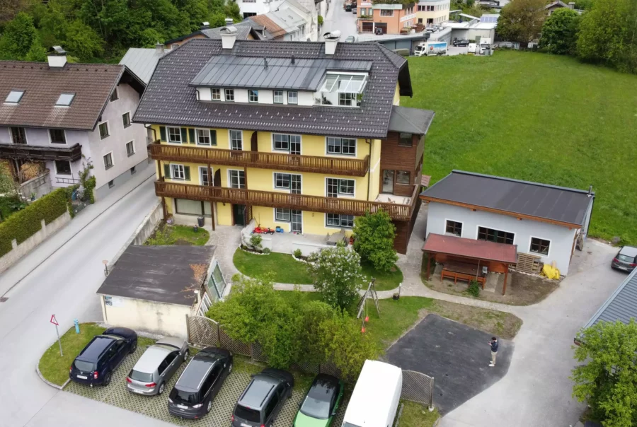 Mehrstöckiges Wohngebäude mit gelber Fassade, Parkplätzen und angrenzendem Grünbereich in Werfen, Salzburg.