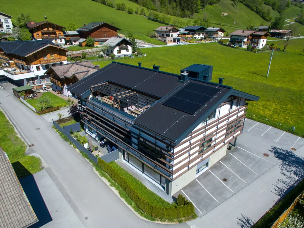 deutinger-projektentwicklung-baumanagement-generalunternehmen-immobilien-salzburg-wohnhaus-rohrmoser-02 Modernes Wohnhaus mit Solarpanelen auf dem Dach in ländlicher Umgebung mit grünen Wiesen und weiteren Häusern in Rohrmoser