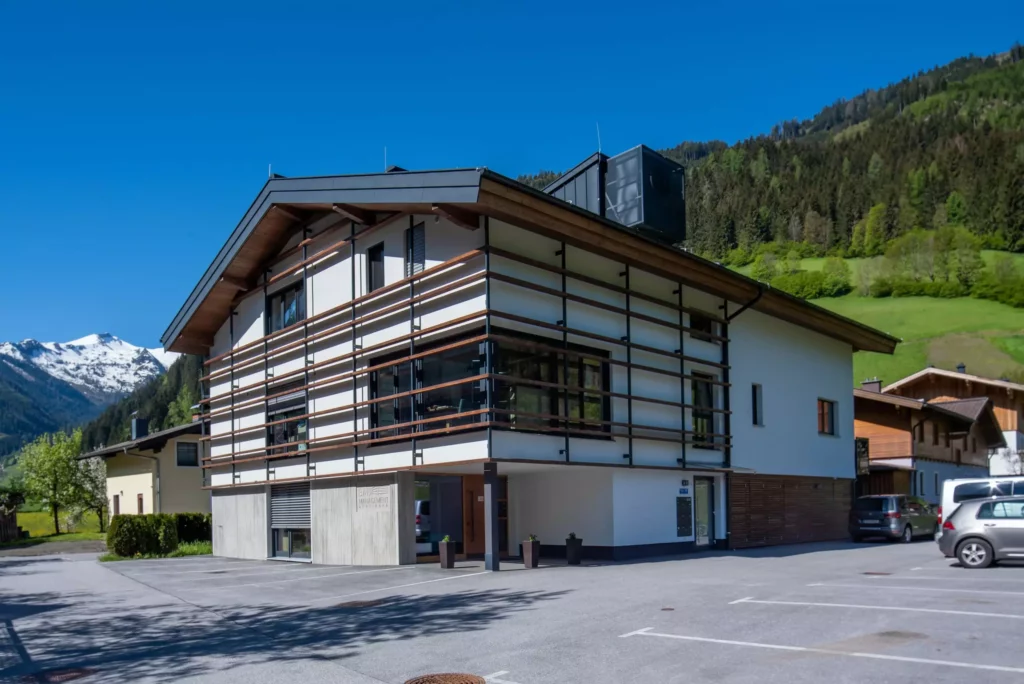 deutinger-projektentwicklung-baumanagement-generalunternehmen-immobilien-salzburg-wohnhaus-rohrmoser-04 Modernes Wohnhaus mit Holz- und Glasfassade vor Bergkulisse und blauem Himmel in Rohrmoser, Salzburg