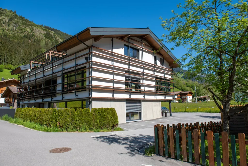 deutinger-projektentwicklung-baumanagement-generalunternehmen-immobilien-salzburg-wohnhaus-rohrmoser-06 Modernes Wohnhaus mit Holzverkleidung und großem Parkplatz in ländlicher Berglandschaft bei Rohrmoser, Salzburg