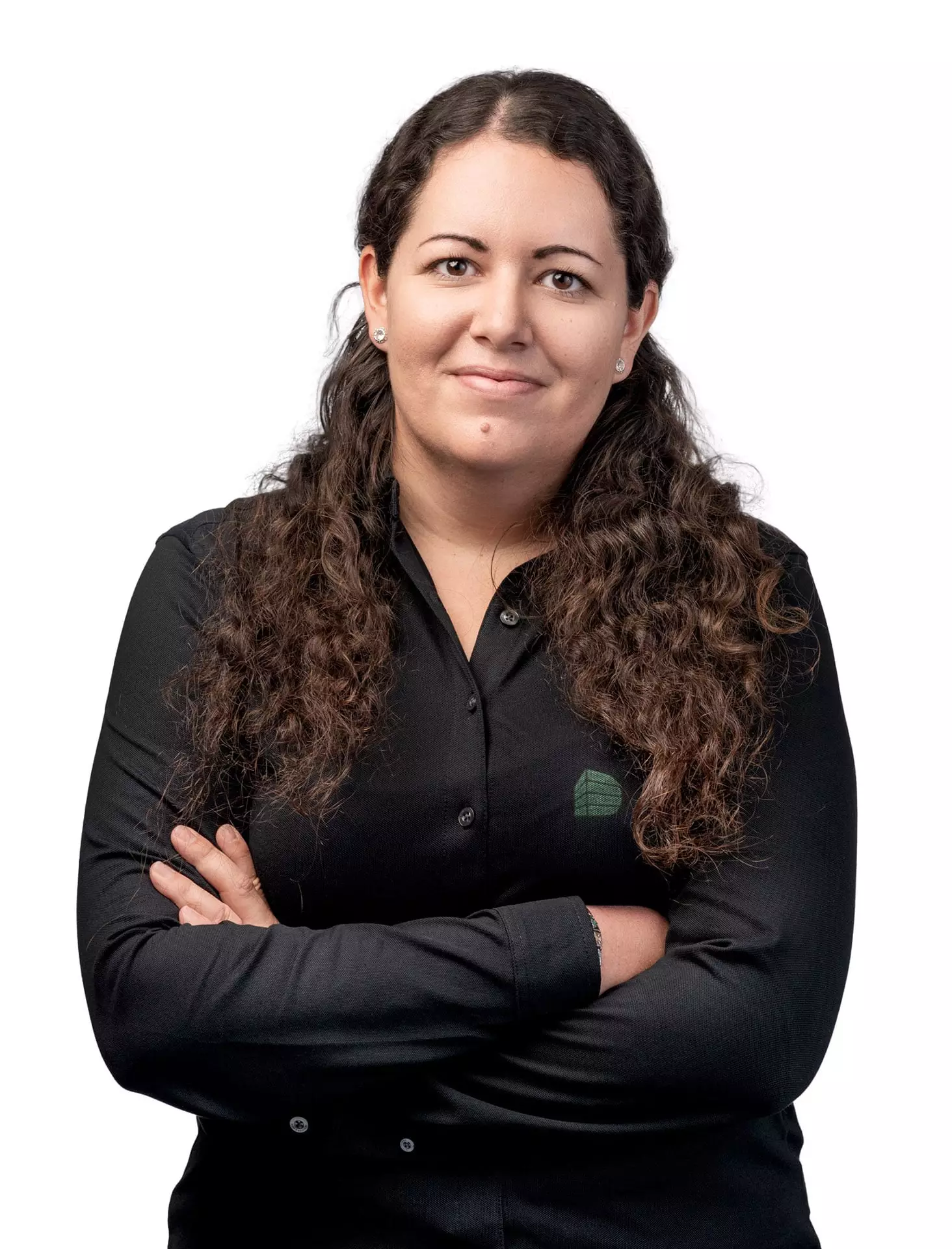 Porträt einer Frau mit langen lockigen braunen Haaren, schwarzem Hemd und verschränkten Armen vor weißem Hintergrund