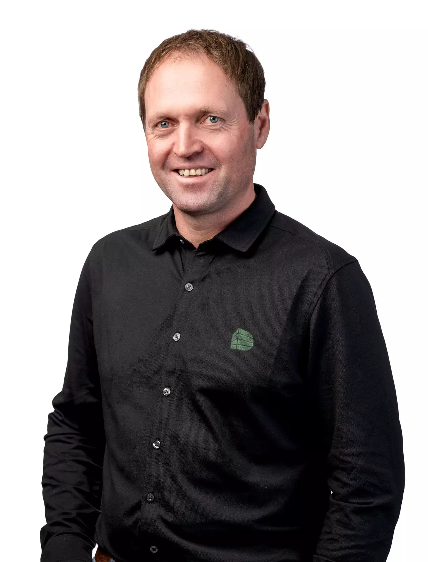 Porträt eines lächelnden Mannes in schwarzem Hemd mit grünem Logo vor weißem Hintergrund, Baumanagement-Teammitglied Michael