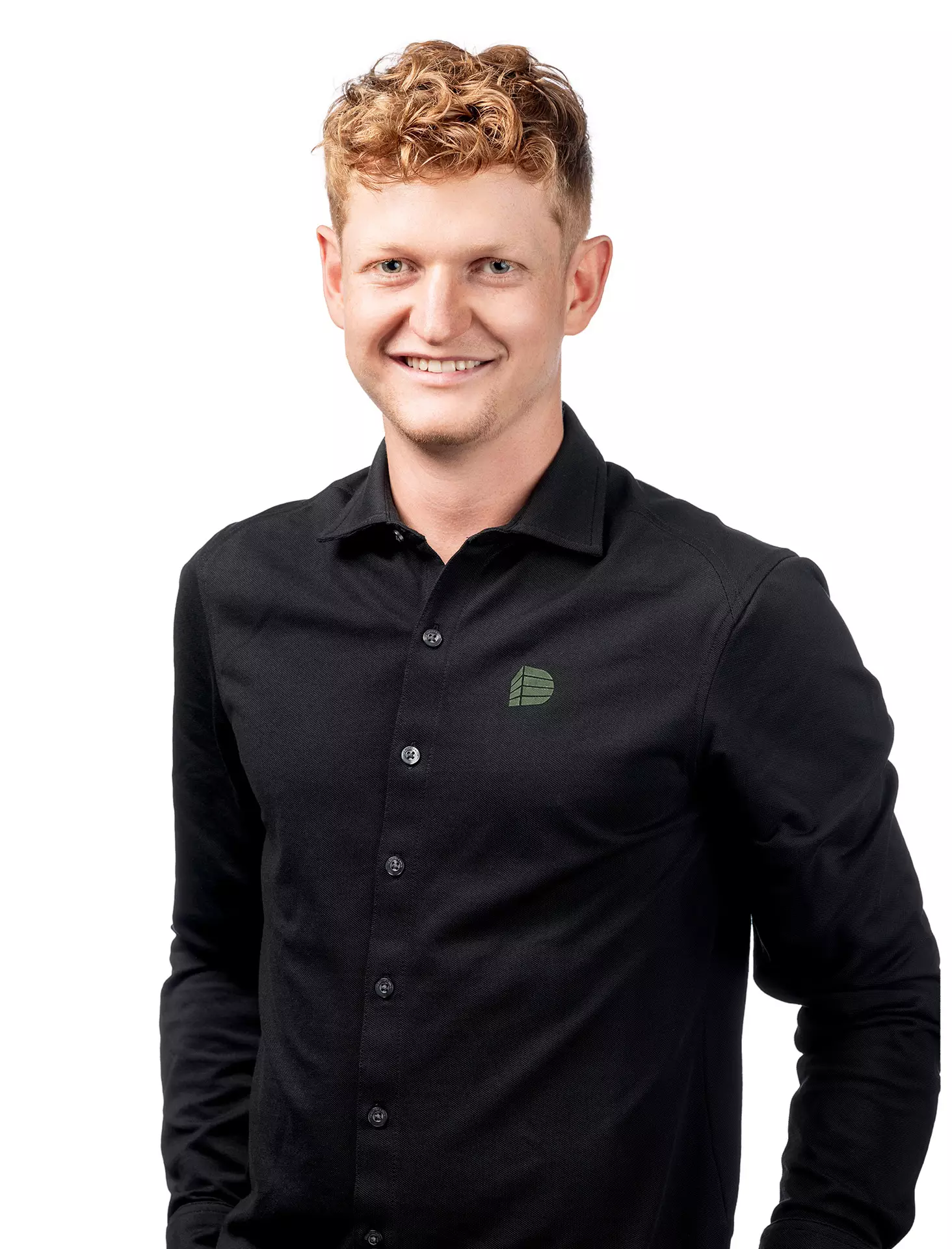 Junger Mann mit lockigem roten Haar trägt schwarzes Hemd mit grünem Logo vor weißem Hintergrund, Porträtfoto für