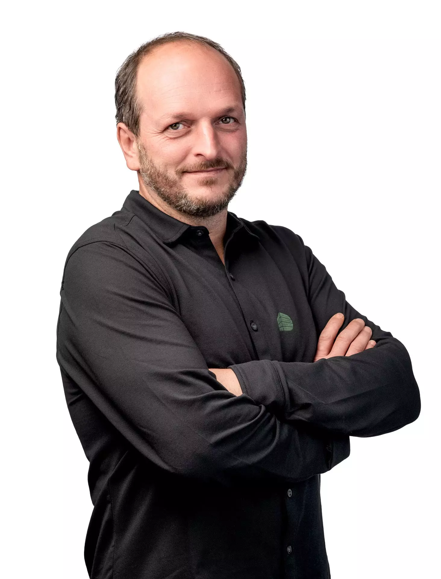 Porträt eines Mannes mit Bart und schwarzem Hemd vor weißem Hintergrund, Arme verschränkt, freundlich blickend