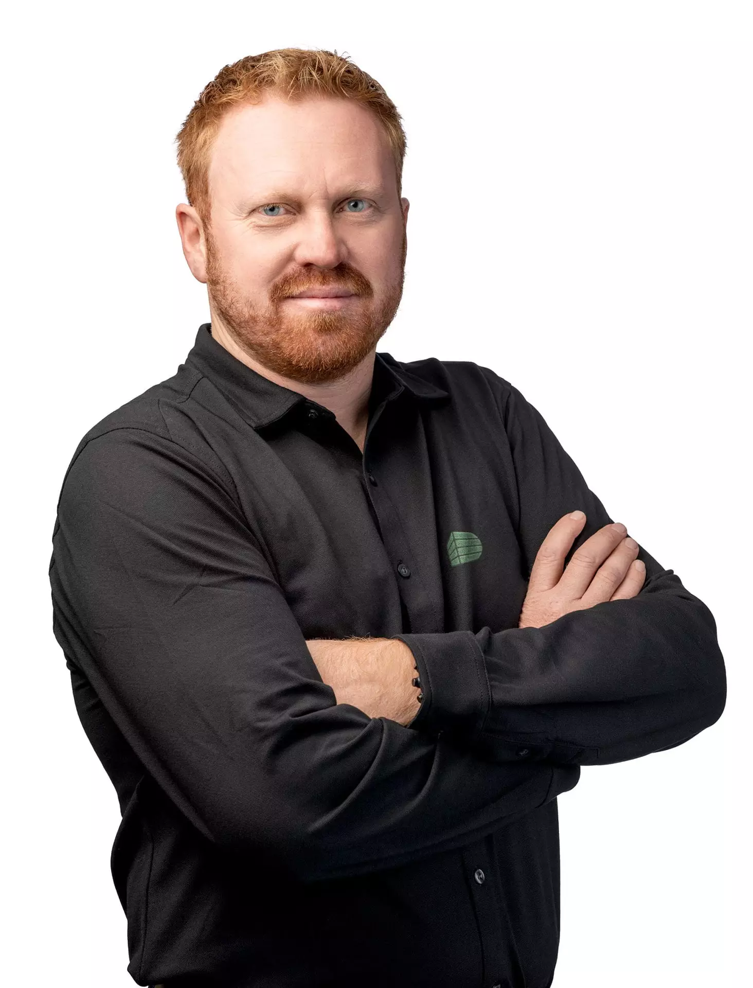 Porträt eines Mannes mit rotem Haar und Bart in schwarzem Hemd mit verschränkten Armen vor weißem Hintergrund