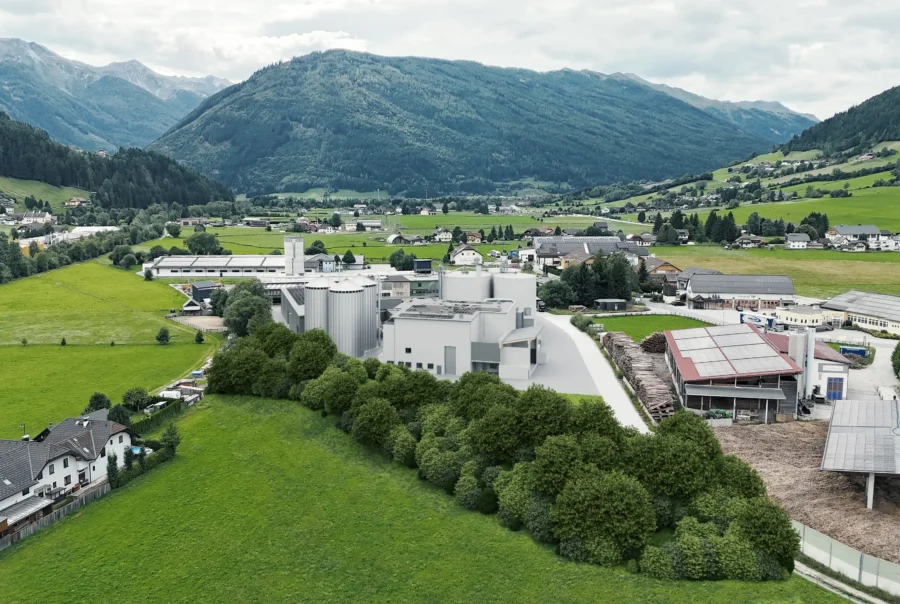 Luftaufnahme eines Industriegebiets mit modernen Gebäuden, umgeben von grünen Wiesen und Bergen im Hintergrund