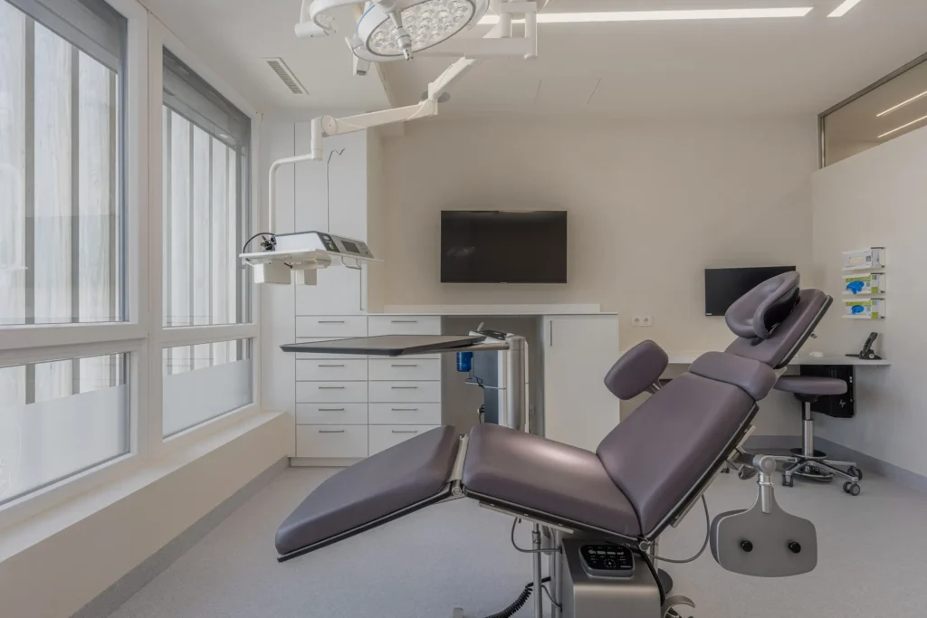 260526_Deutinger-DrNachtigal-©sobietzki-low-14 Moderner Behandlungsraum mit verstellbarem Behandlungsstuhl, medizinischer Lampe und Monitor an der Wand im