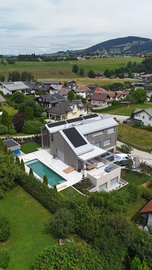 01_EFH Salzkammergut Modernes Einfamilienhaus mit Pool und Solarpaneelen im Salzkammergut, umgeben von grüner Landschaft und Nachbarhäusern