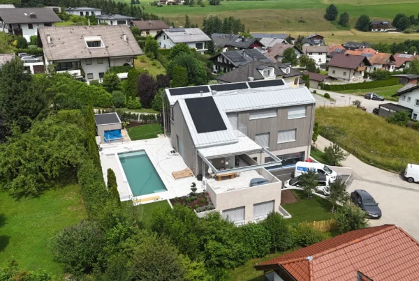 Modernes Einfamilienhaus mit Pool und Solaranlagen im Salzkammergut, umgeben von grüner Landschaft und Nachbarhäusern