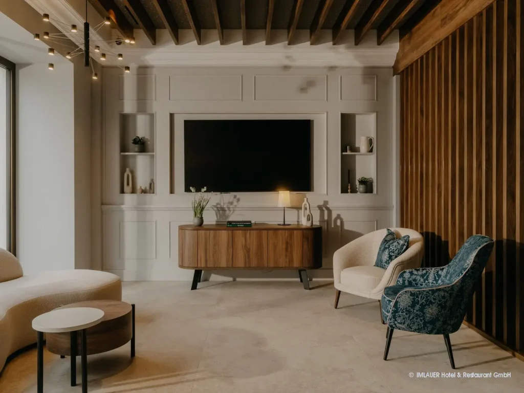 02_ImlauerPalaisMirabell_Copyright IMLAUER Moderner Wohnbereich mit TV, Holzsideboard, zwei Sesseln, Couch und dekorativer Wandverkleidung im Imlauer Palais Mirabell