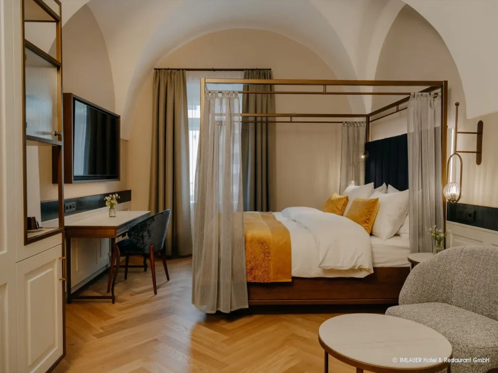 05_ImlauerPalaisMirabell_Copyright IMLAUER Modern eingerichtetes Hotelzimmer mit Himmelbett, Schreibtisch, Fernseher und gemütlicher Sitzecke im Imlauer Palais Mirabell